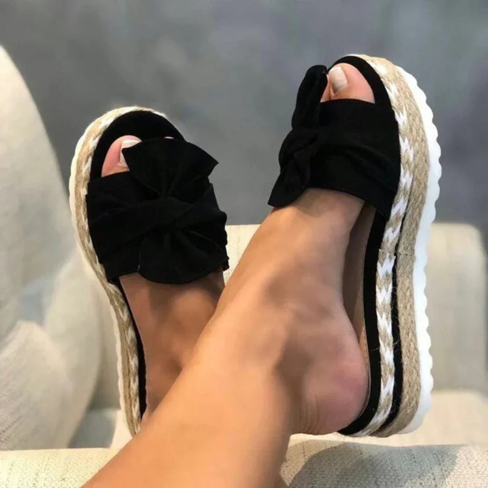 Women black bow accent platform slide sandals with braided sole detail, side view on feet