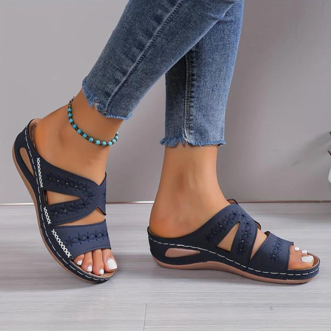 Women navy slip-on sandals with white floral stitching and open toe worn with jeans