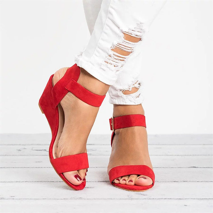 Women red open toe wedge sandals with ankle strap and buckle closure on a model wearing white jeans.