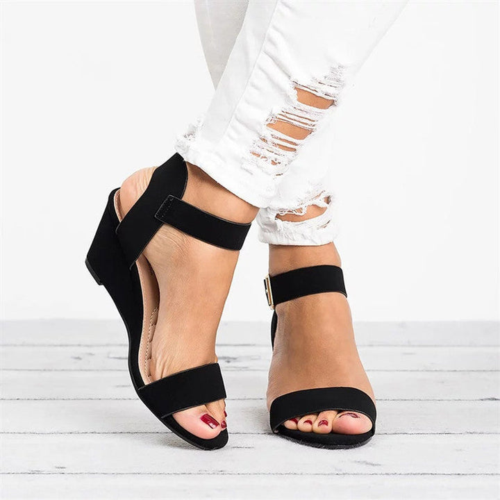 Women black open toe wedge sandals with adjustable ankle strap closure on a model wearing ripped white jeans.