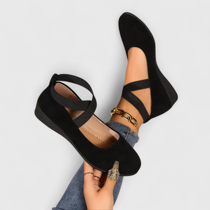 Women black strappy round toe wedge flats on mannequin foot with jeans, displaying elastic ankle straps.