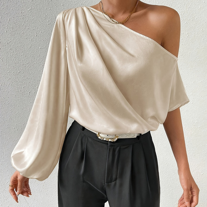 Women's ivory off-shoulder one-sleeve top, draped design, model posing with hands in pockets.