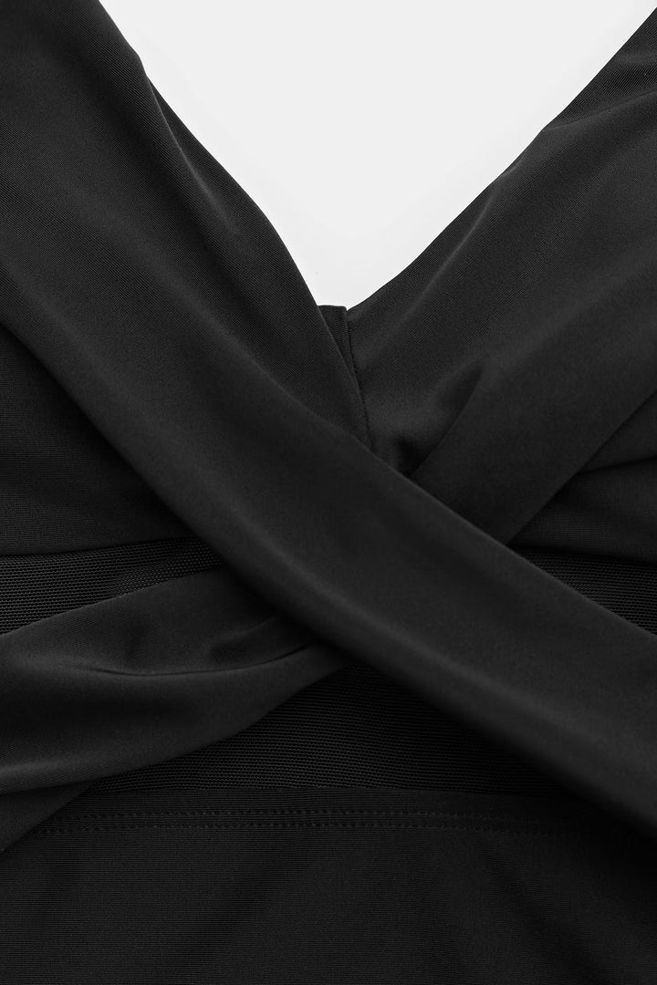 Detail of the black swimsuit's crossover V-neckline and mesh waist panel