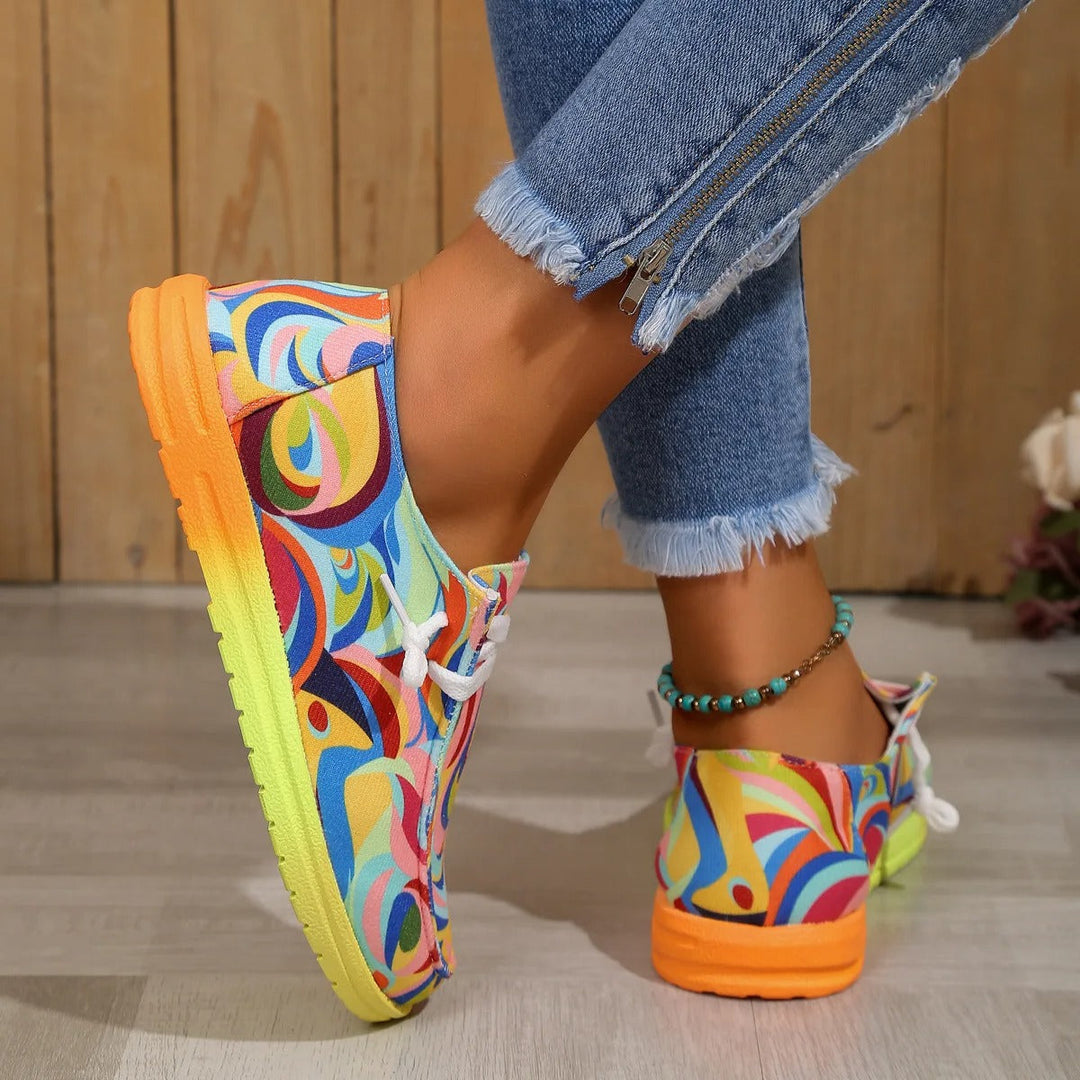 Women's printed low top sneakers with an orange and green gradient sole, worn with blue jeans.