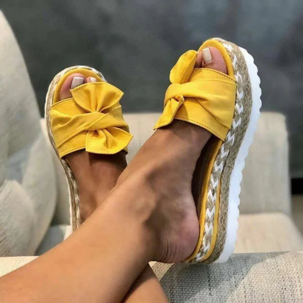 Women yellow bow accent platform slide sandals with textured sole, close up on feet