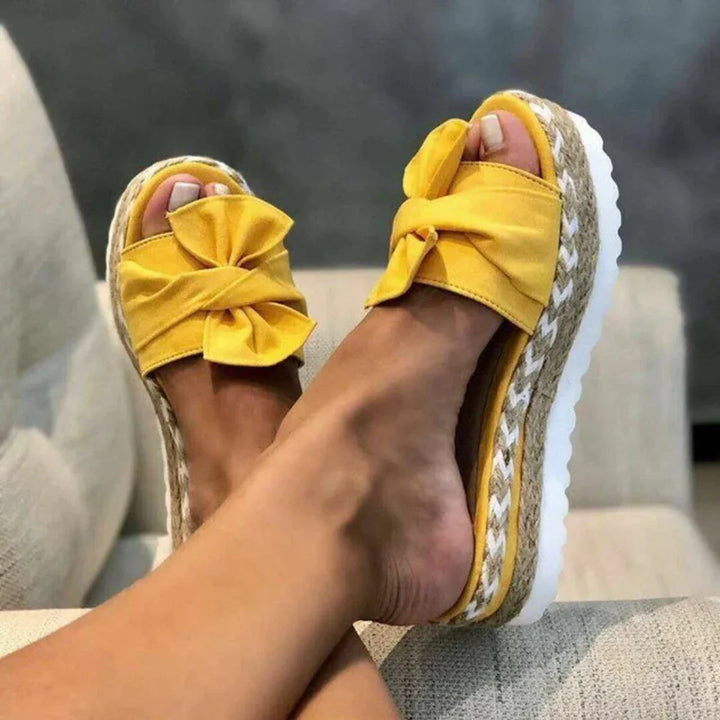 Women yellow bow accent platform slide sandals with textured sole, close up on feet