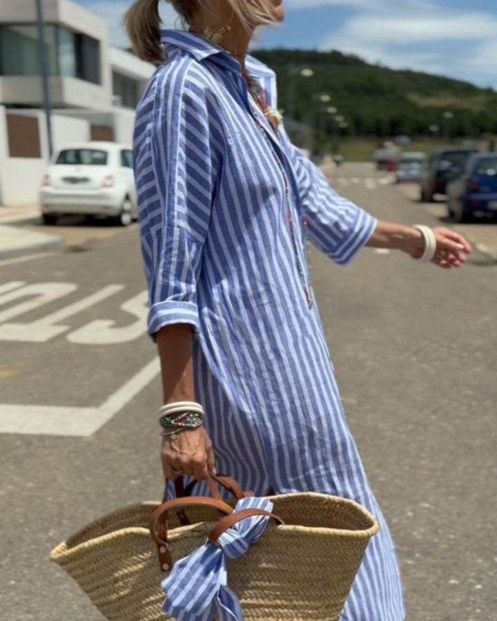 Women striped blue and white maxi shirt dress walking on street, side view.