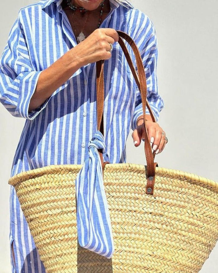 Women hands holding straw bag, striped blue and white button down maxi shirt dress detail.