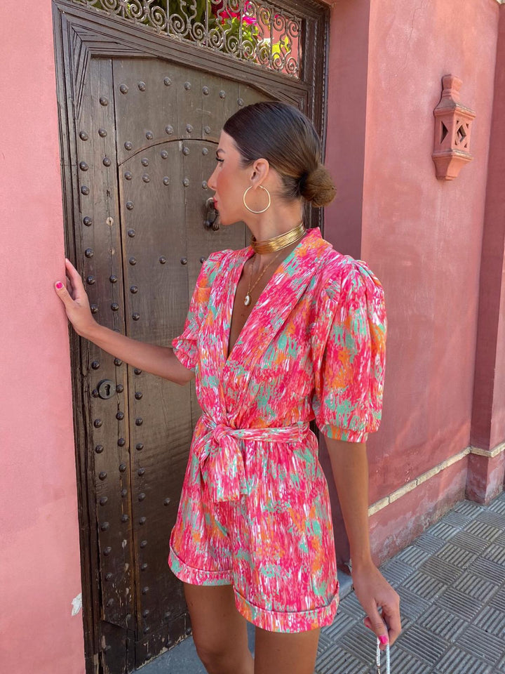 Women's pink printed short sleeve romper with a tie-front closure and cuffed shorts, side profile.