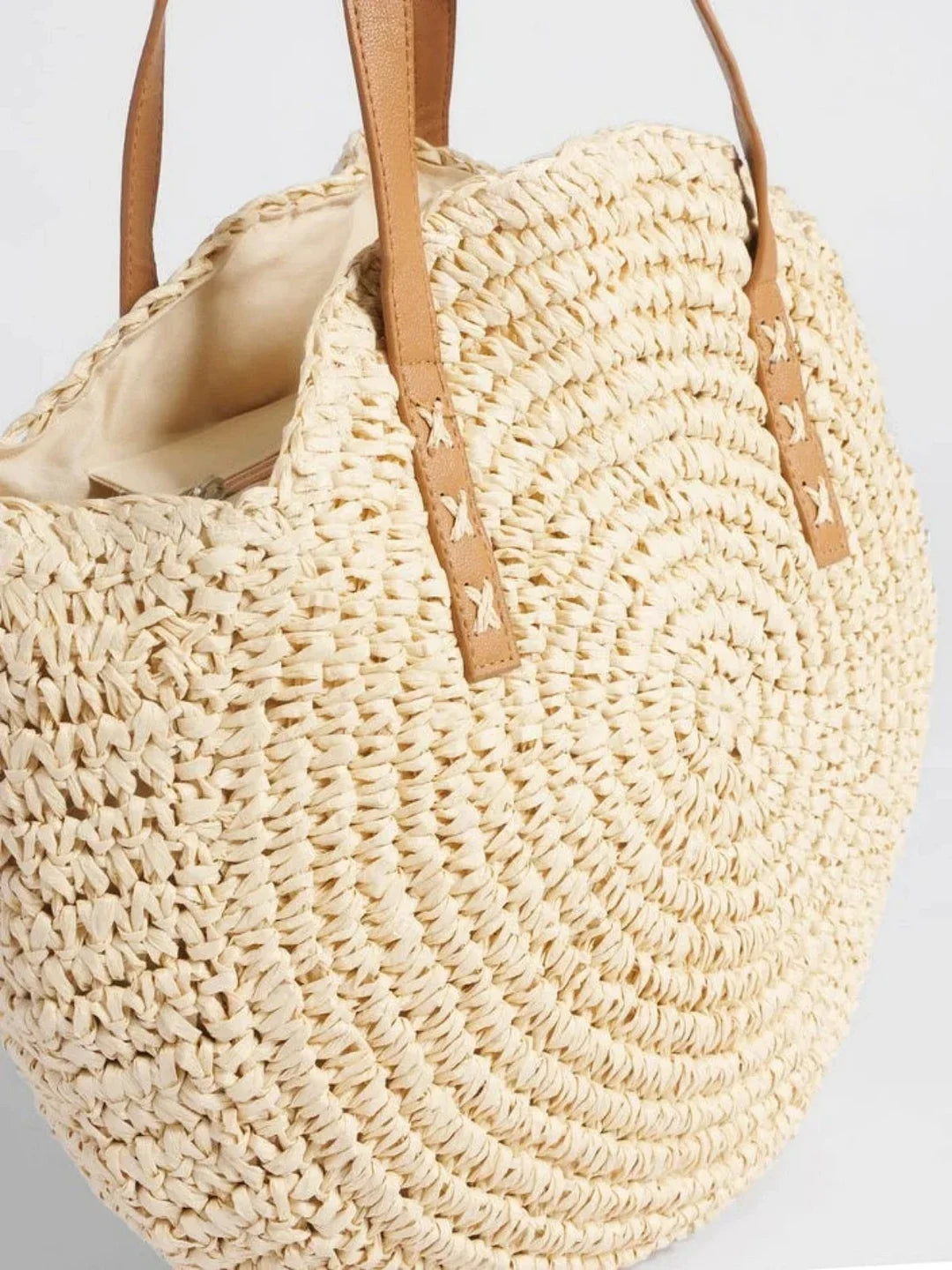 Close up view of women woven straw round tote bag highlighting texture and open top lining