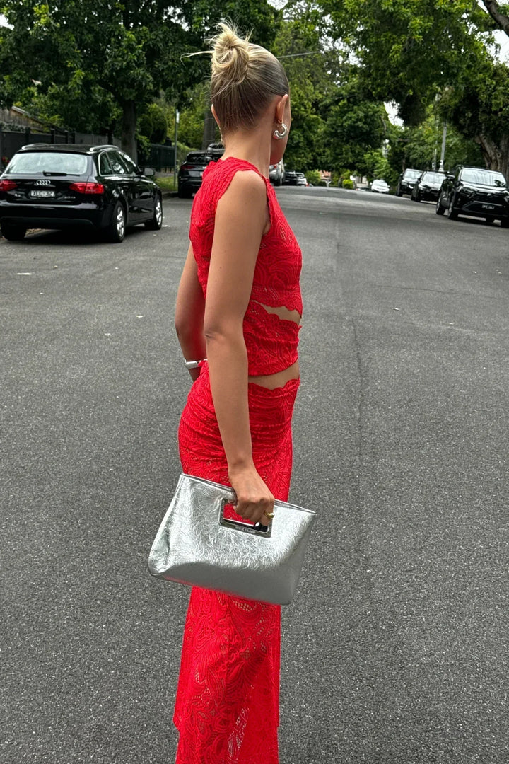 Women red sleeveless lace midi skirt set with high side split from the side view, carrying silver bag.