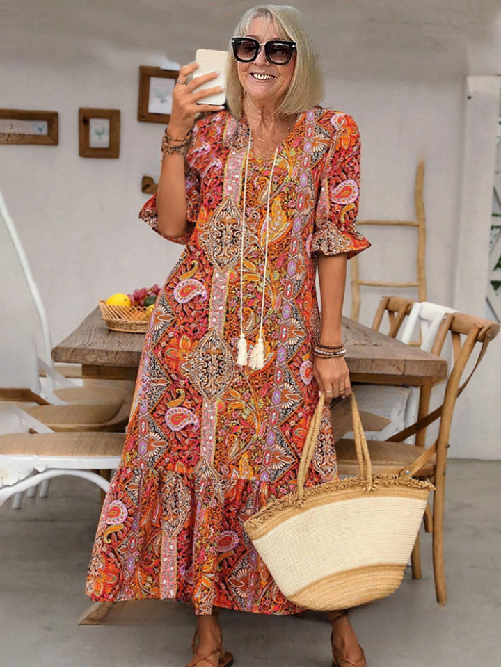 Women red-orange printed midi dress with lace-up V-neck and short ruffled sleeves, front view with straw bag.
