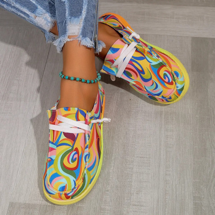 Top-down view of women's colorful printed low top sneakers with white laces and a yellow-orange sole.