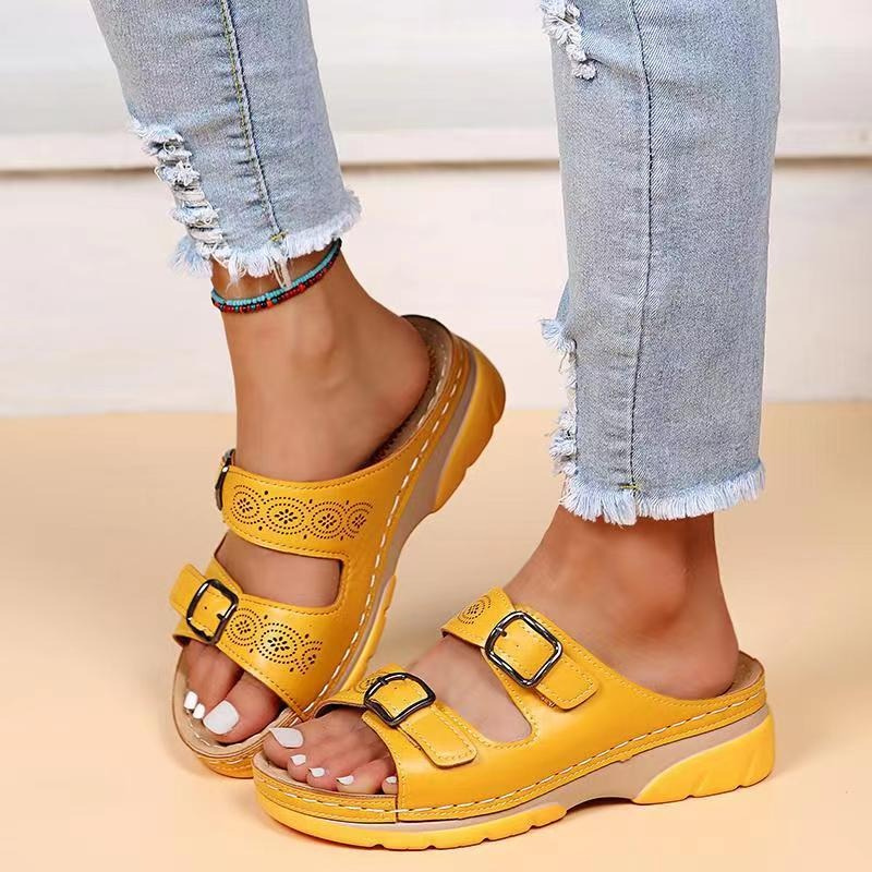 Women's yellow laser cut buckle flat sandals on model's feet, facing forward