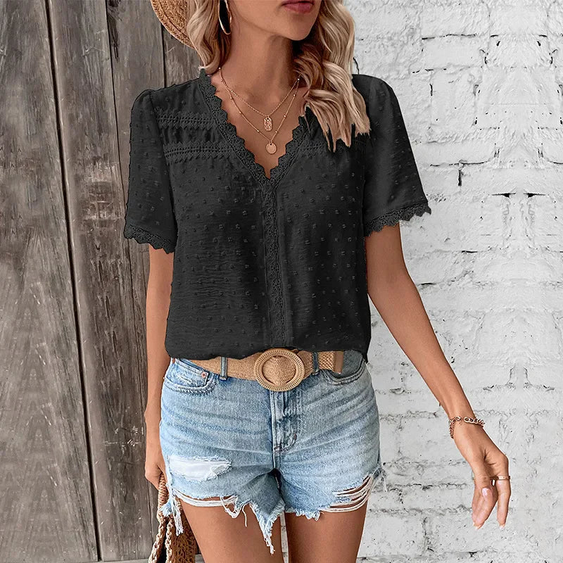 Women black swiss dot V-neck short sleeve blouse with lace trim on a white brick background