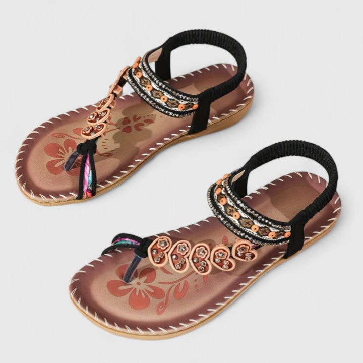 Pair of women's dark color flat sandals with floral sole, beaded strap, elastic back