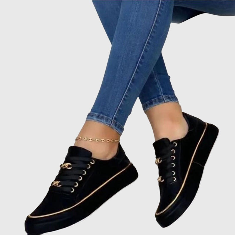 Women black platform lace up sneakers with metallic chain-link eyelets and gold trim on sole, worn with jeans.