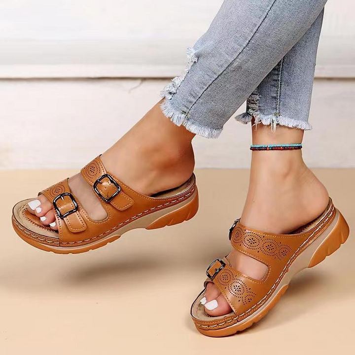 Women's brown laser cut buckle flat sandals on model's feet with light-wash jeans