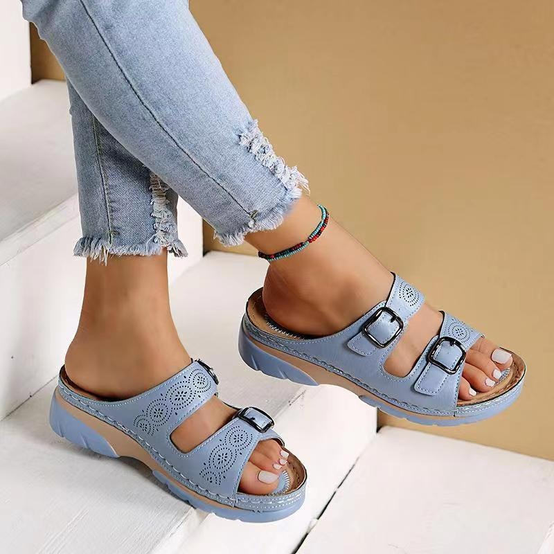 Women's light blue laser cut buckle flat sandals on model's feet on stairs