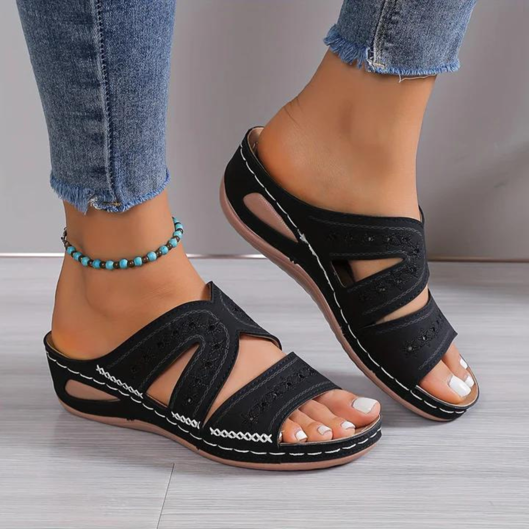Women black slip-on sandals with white stitching and cut-out details worn with distressed jeans