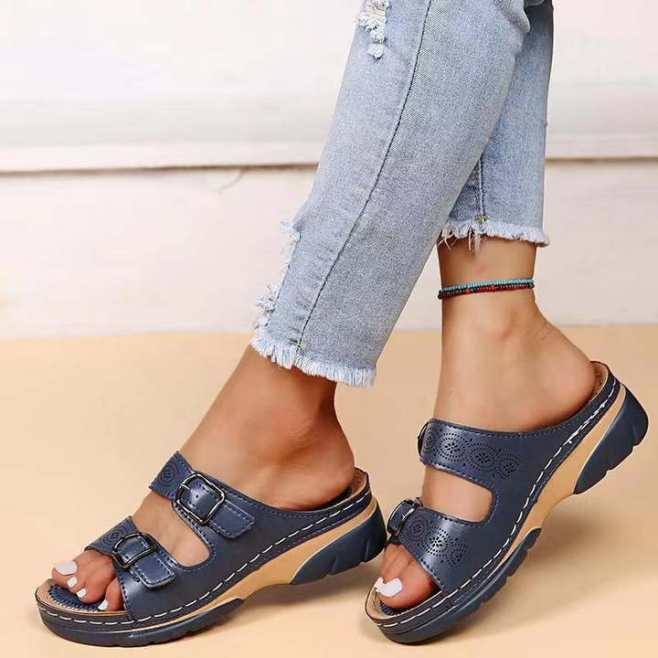 Women's blue laser cut buckle flat sandals on model's feet with ripped jeans