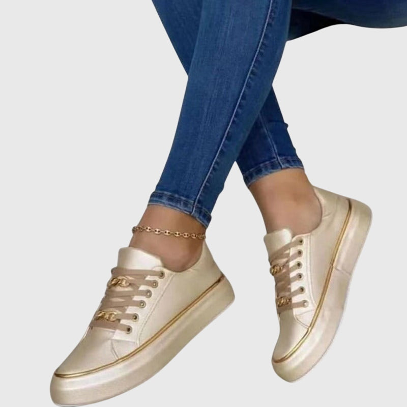 Women light gold platform lace up sneakers with metallic chain-link eyelets and gold trim on sole, worn with jeans.