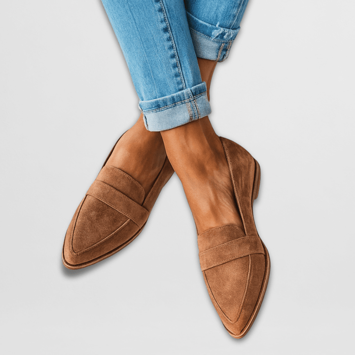 Women brown suede pointed toe loafers worn with blue cuffed jeans, crossing legs