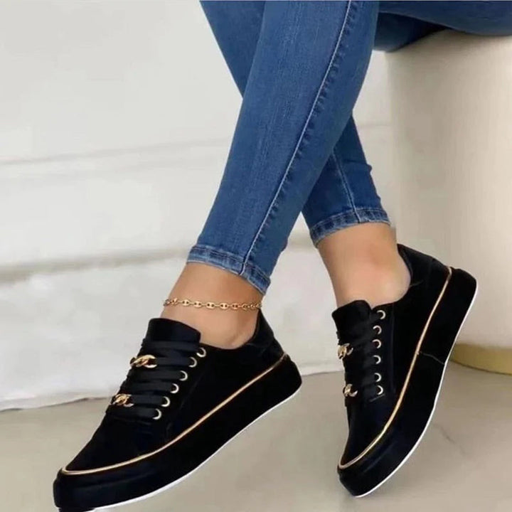 Women black low top sneakers with gold chain laces and gold trim on model's feet