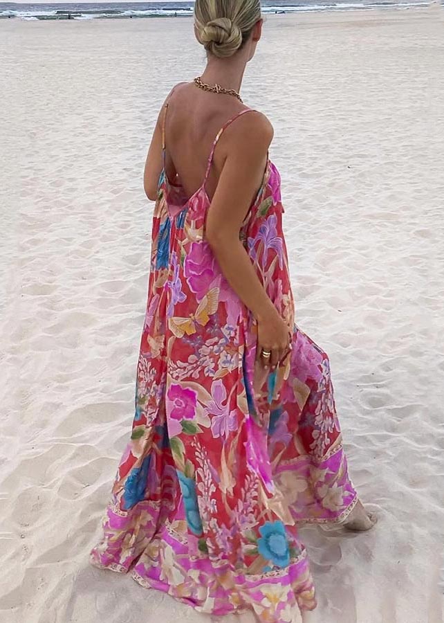 Women's red floral print maxi sundress with low back and spaghetti straps walking on sand.
