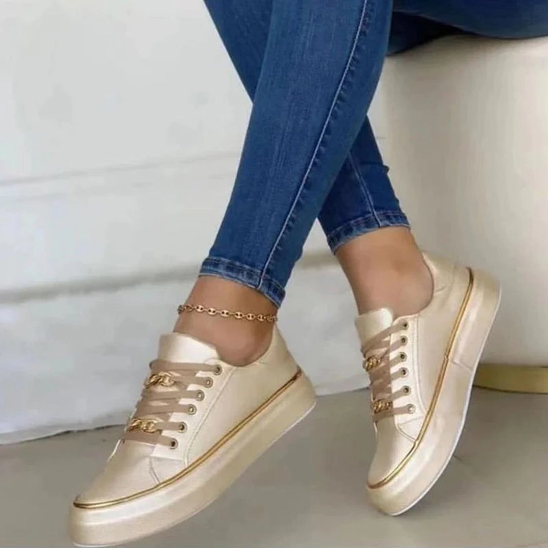 Women beige low top platform sneakers with gold chain laces and gold trim on model's feet