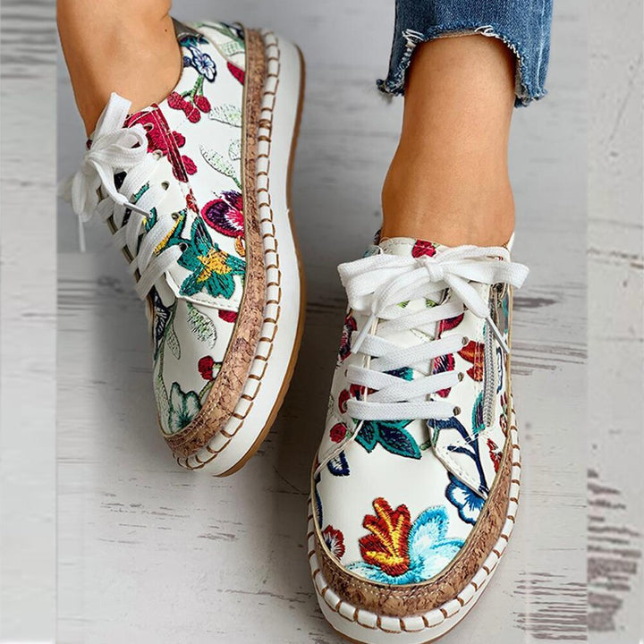 Women's feet wearing white floral print sneakers with laces and side zipper, styled with jeans