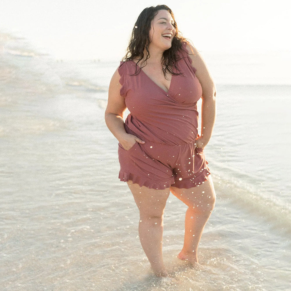 Women berry sleeveless romper with V-neckline standing in shallow water, showing ruffle detail