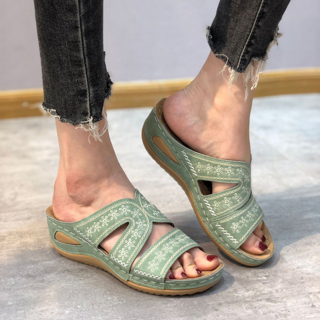 Women green slip-on sandals with white floral embroidery and open toe worn with dark jeans