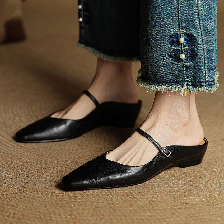 Women black slip-on mules with buckle strap worn on feet with denim jeans