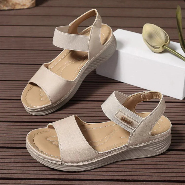Pair of beige adjustable strap open-toe sandals with cushioned sole on wood floor