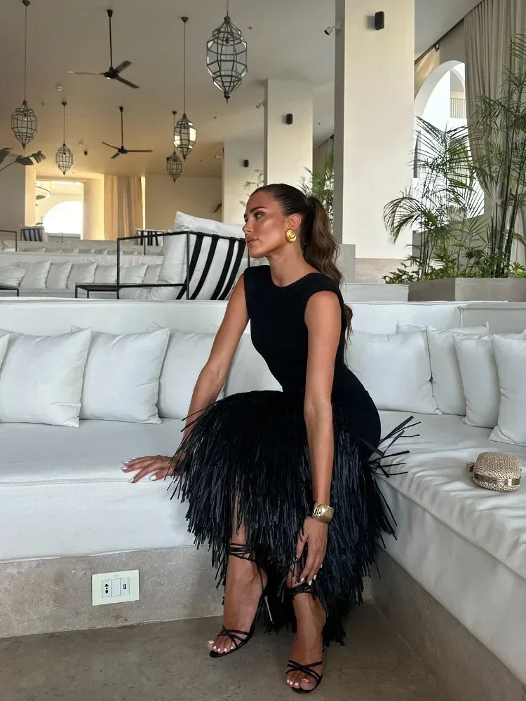 Women black sleeveless feathered midi dress on model, side view seated on white sofa