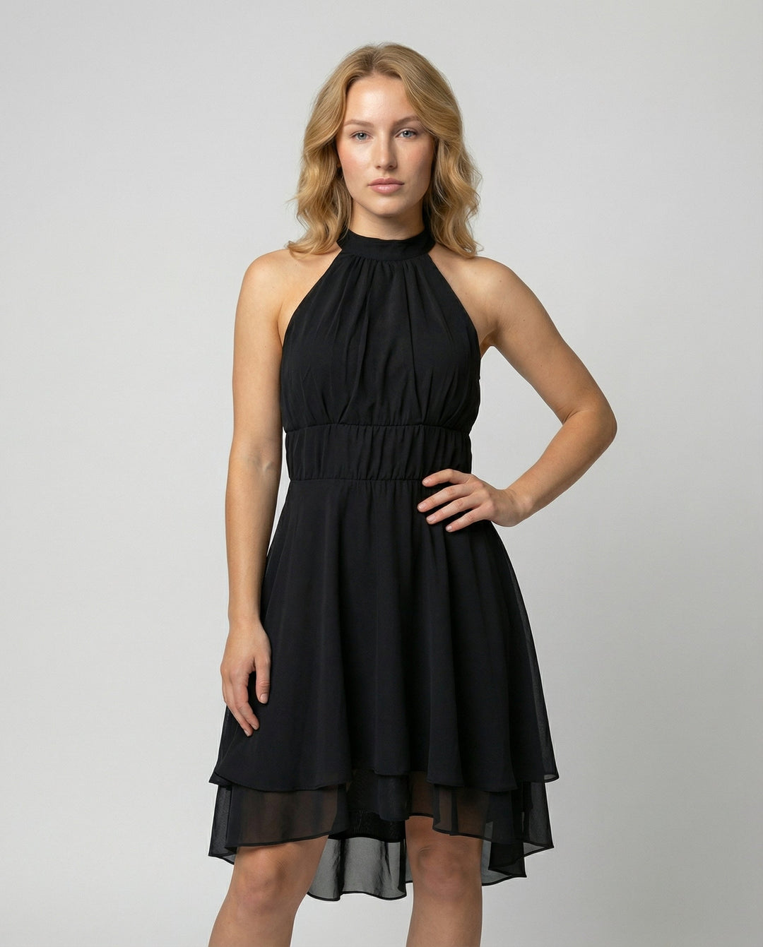 Women black halter neck mini dress with layered ruffle skirt and cinched waist, model standing.
