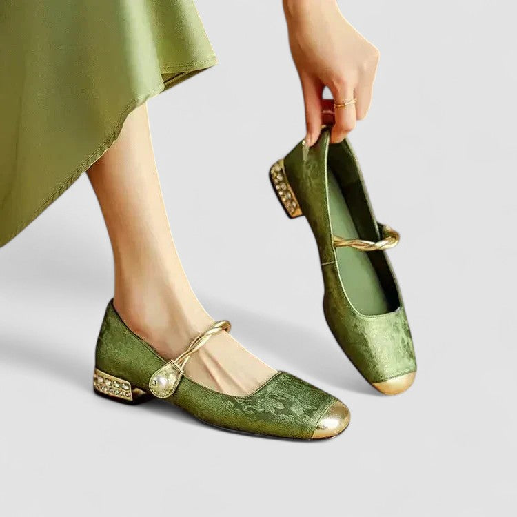 Women green Mary Jane shoes with square metallic toe and decorative heel; model is seated with one shoe on and one in hand.