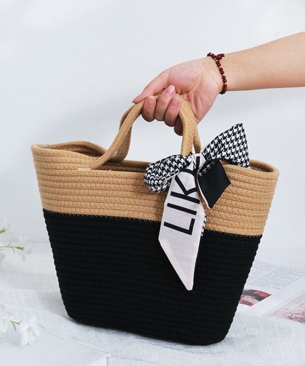 Women's hand holding the beige and black woven tote bag, showcasing the dual top handles.