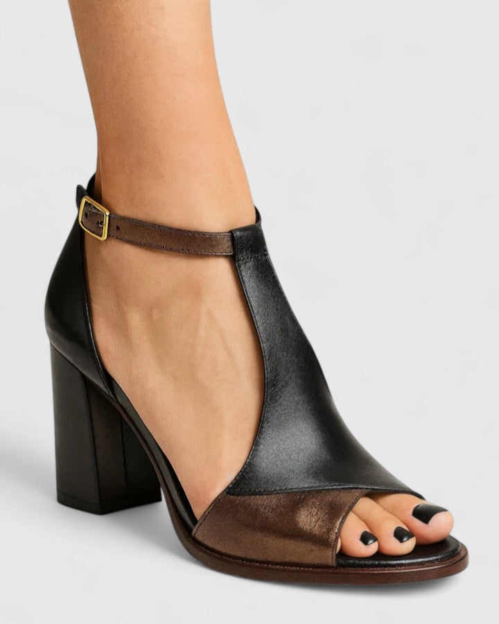 Women two-tone black and bronze block heel sandal with T-strap and ankle strap, model wearing.