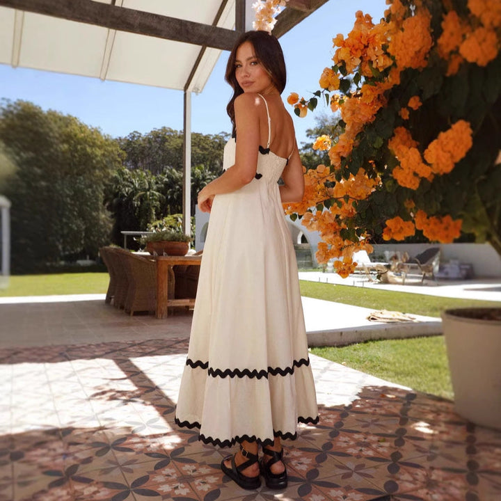 Women cream A-line spaghetti strap maxi dress with black scalloped trim, back view outdoors