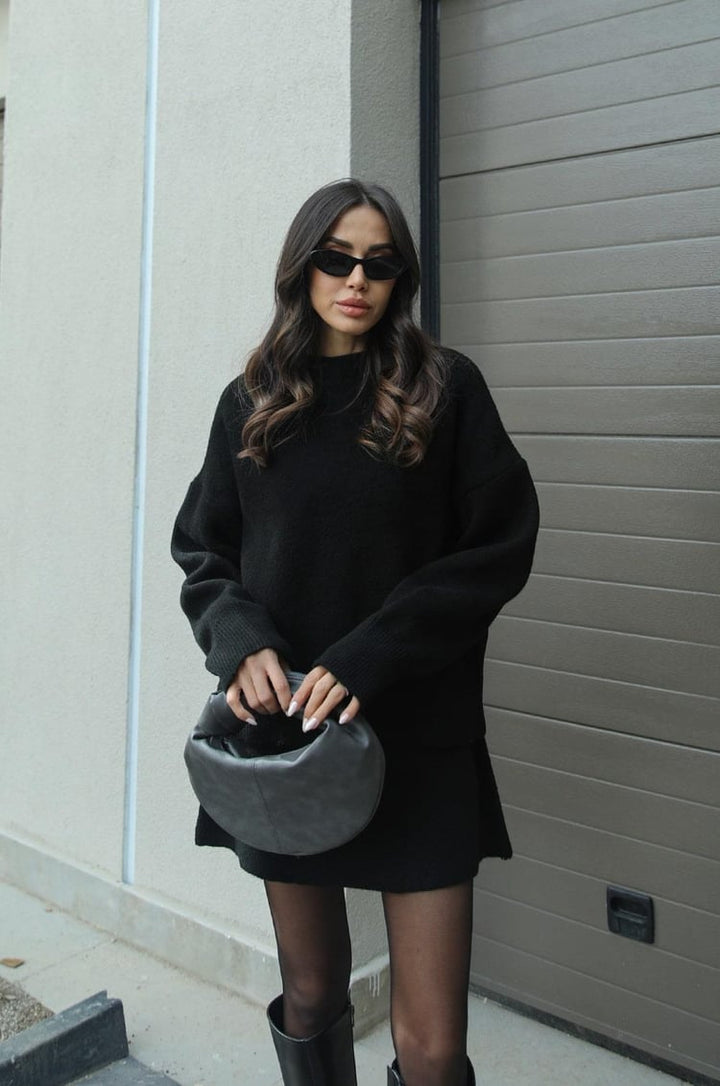 Women black knit crew neck sweater and mini skirt set, side view with handbag
