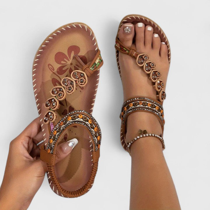 Women's brown flat sandals with beaded toe and strap on model's feet