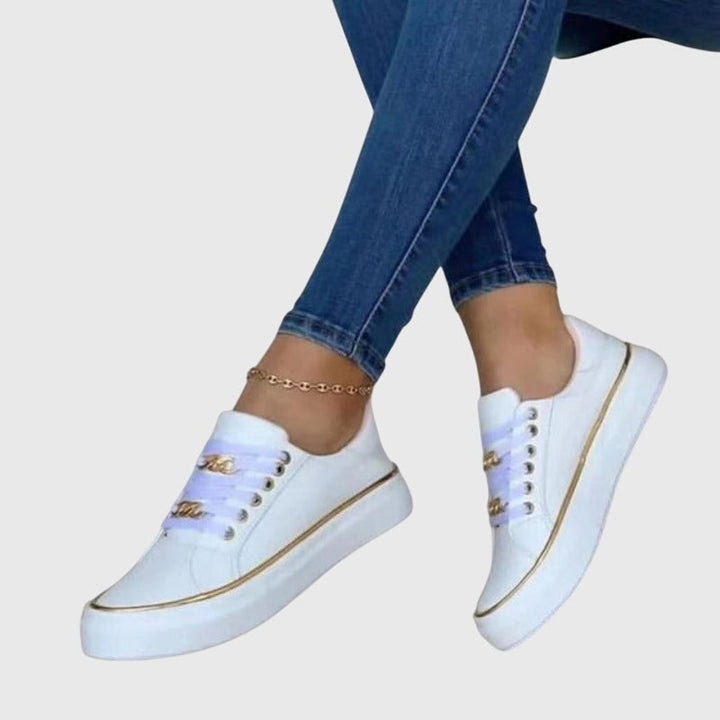 Women white platform lace up sneakers with metallic chain-link eyelets and gold trim on sole, worn with jeans.