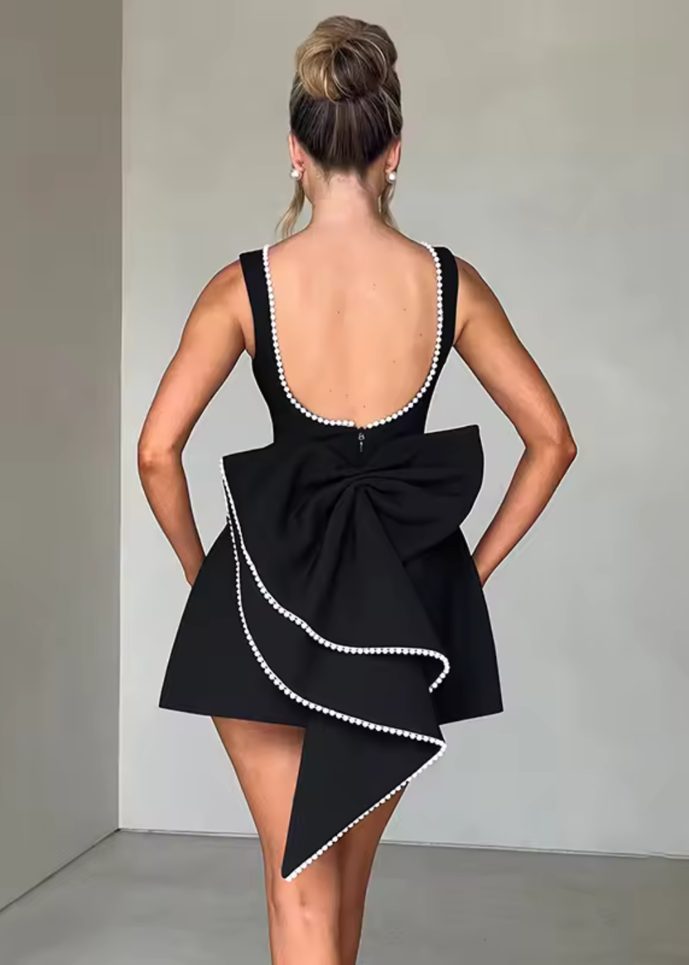 Women black pearl trim mini dress with scoop back and large bow detail, back view.