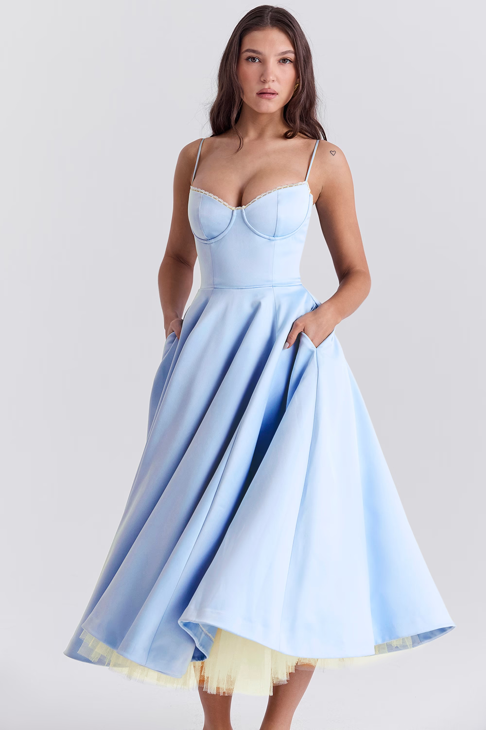 Women light blue bustier midi dress with hands in visible side pockets and voluminous skirt.