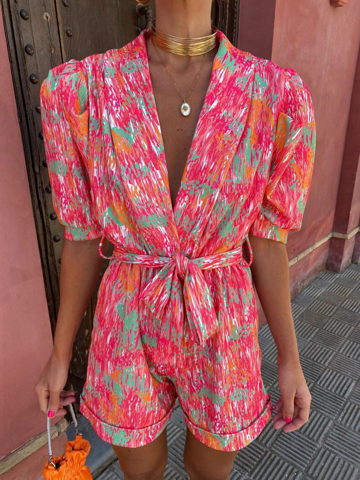 Women's pink geometric metallic printed short sleeve romper with a tie waist, front view.