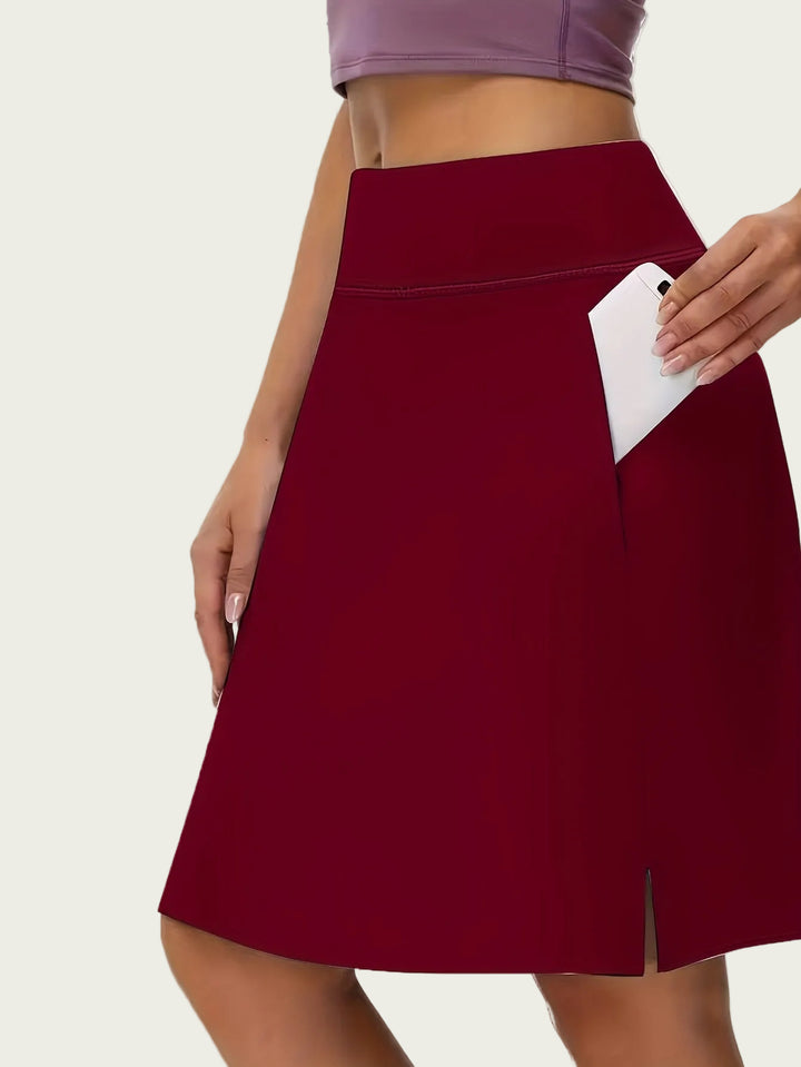 Women burgundy athletic skort with high waist and side pocket holding a phone.