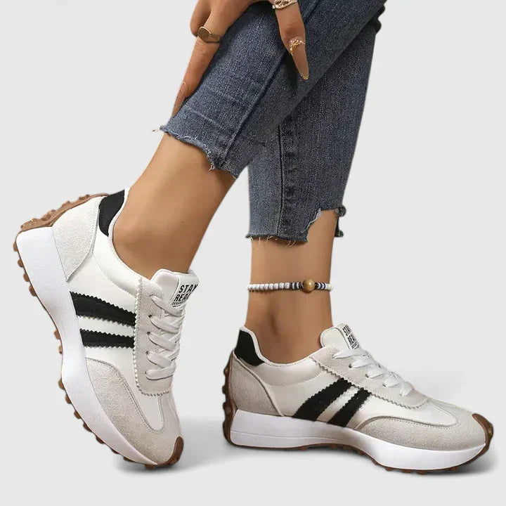 Women's white lace-up sneakers with black stripes, suede-like accents, and textured brown sole detail