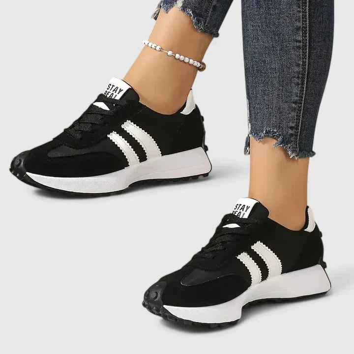 Women's black lace-up sneakers with white stripes, low-top design, and visible white midsole